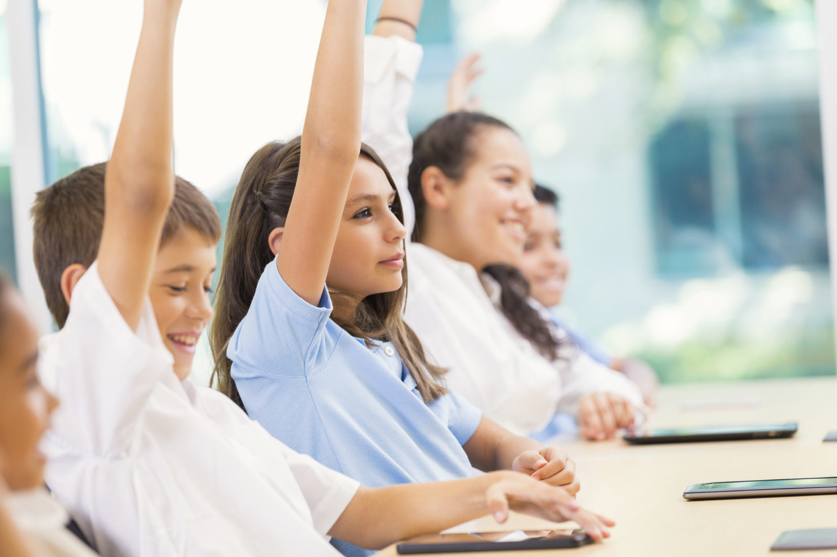 Students in a classroom with their hands up.